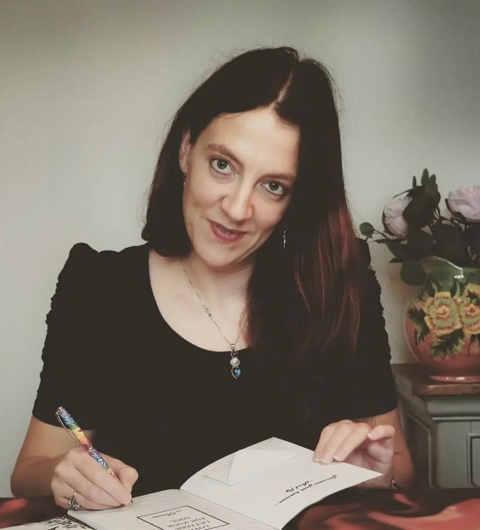 A women with dark hair writing on wooden table a book poetry